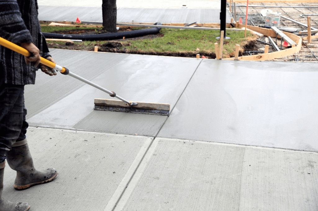 Worker applying a broom finish to a freshly poured concrete sidewalk
