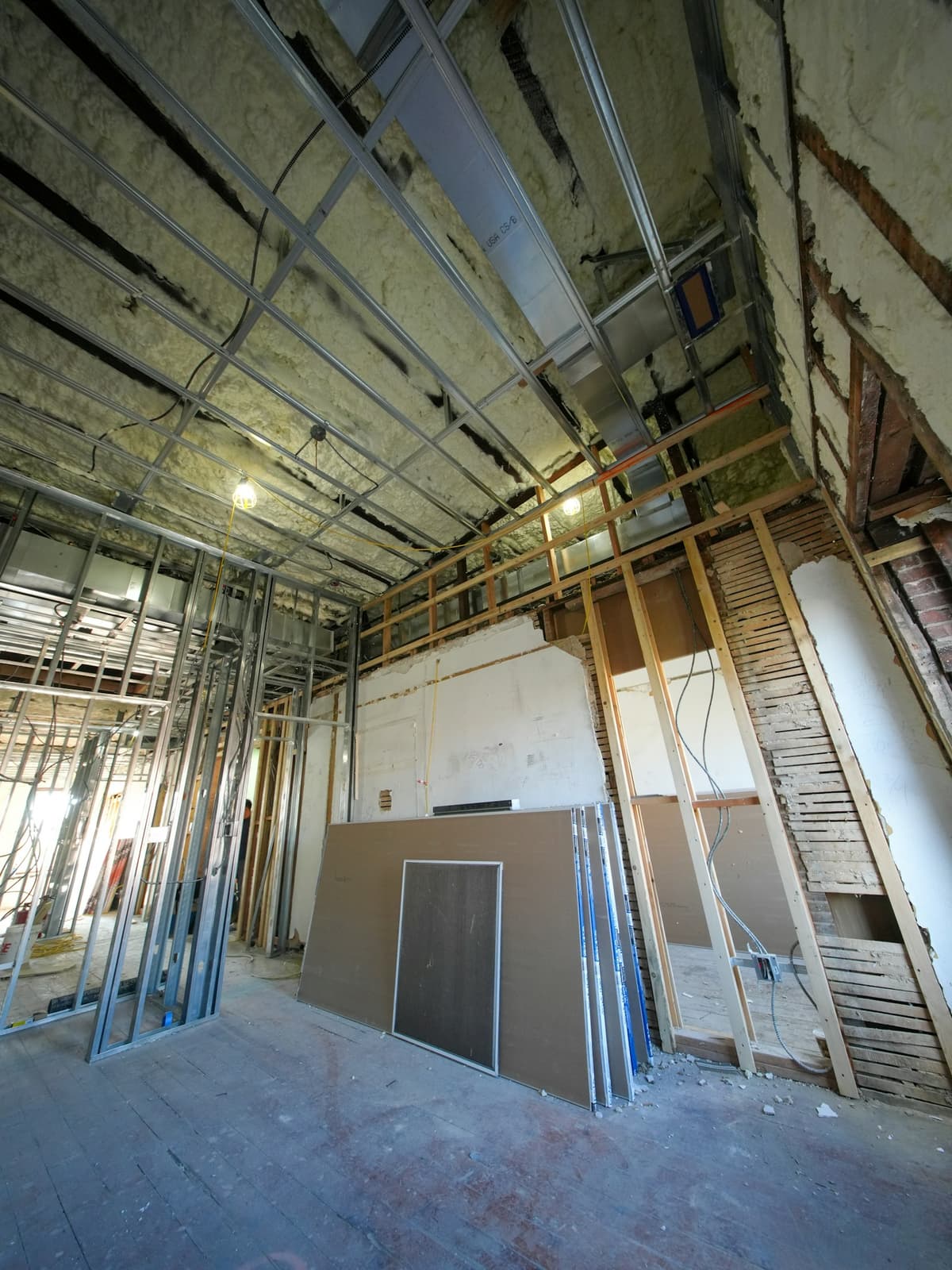 Interior renovation with metal and wood framing, spray foam insulation, and drywall sheets ready to hang